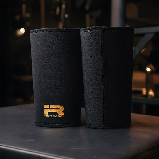 Close-up of a pair of black Iron Rebel PR Cone Knee Sleeves with a gold Iron Rebel logo, highlighting the neoprene material and reinforced stitching. Durable knee compression for powerlifting, squats, and maximizing your PR (Personal Record).